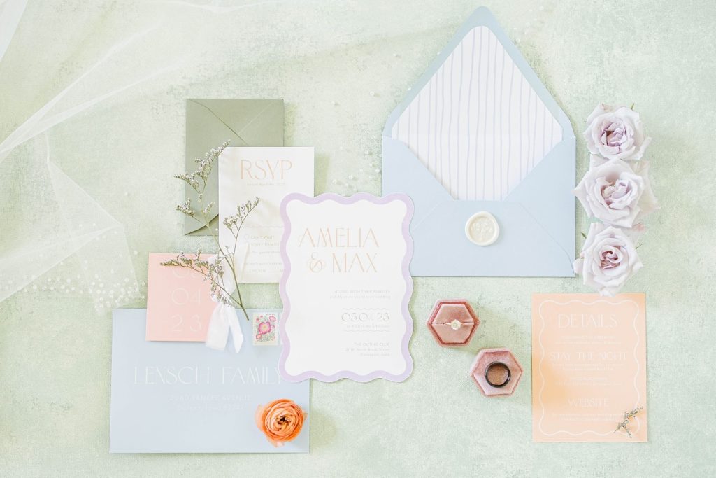 Pastel wedding invitation suite featuring blue envelopes, blush and lavender cards, hexagonal ring boxes, and roses