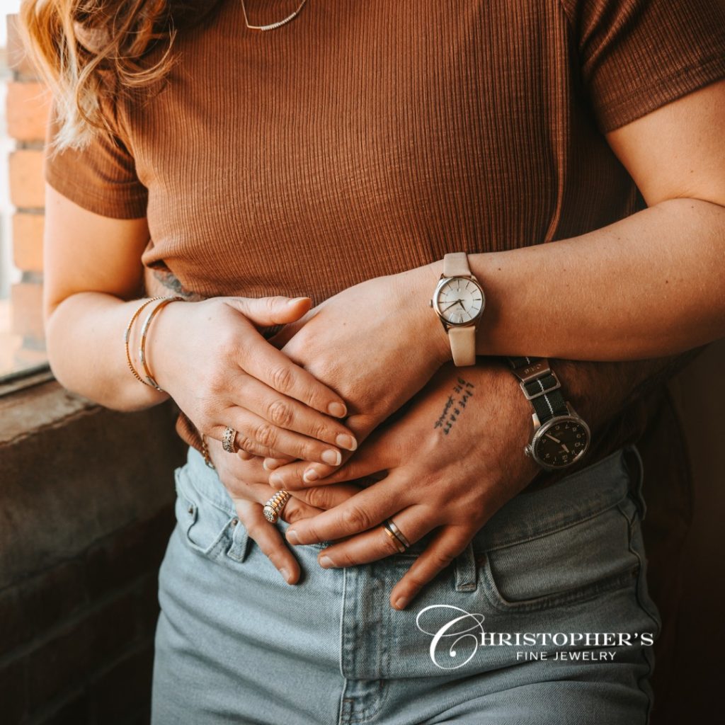 Couple's hands clasped together showing engagement ring and matching watches