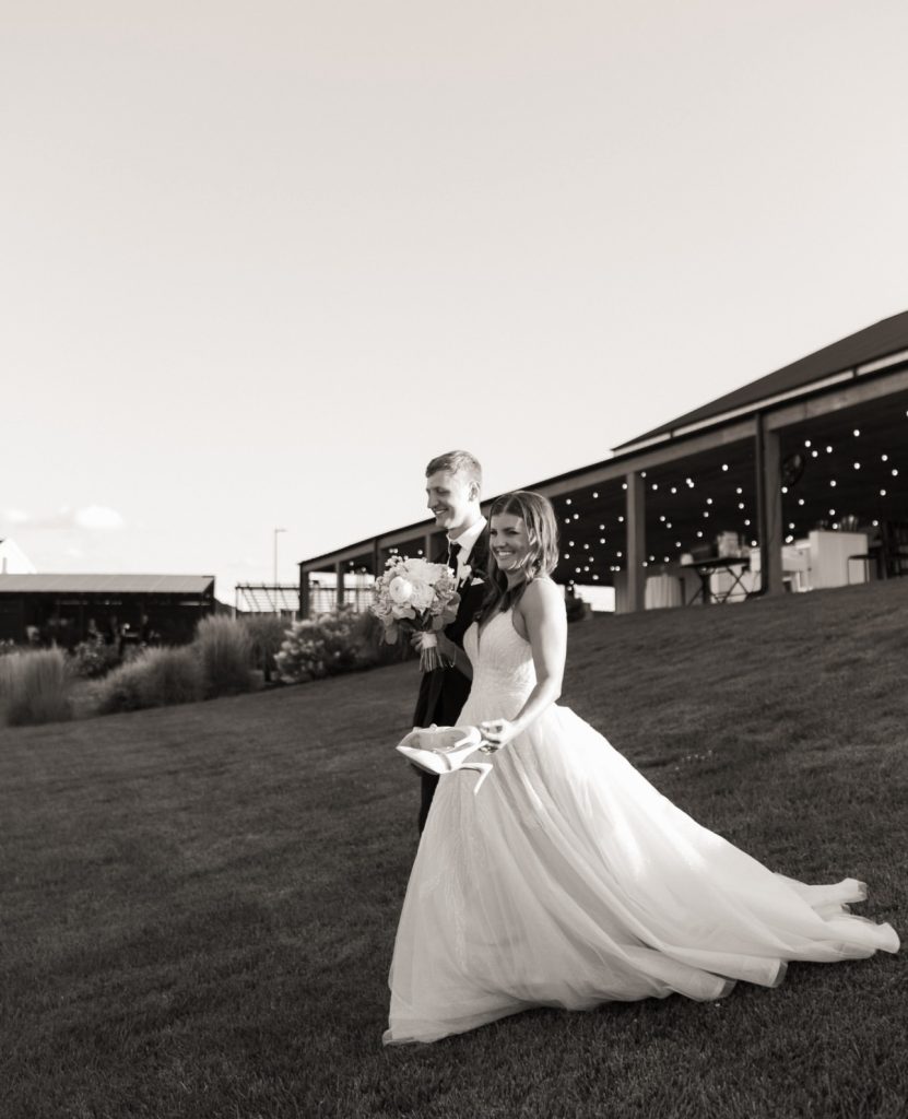 Bride's ballgown sweeps across lawn as couple walks away from modern barn venue
