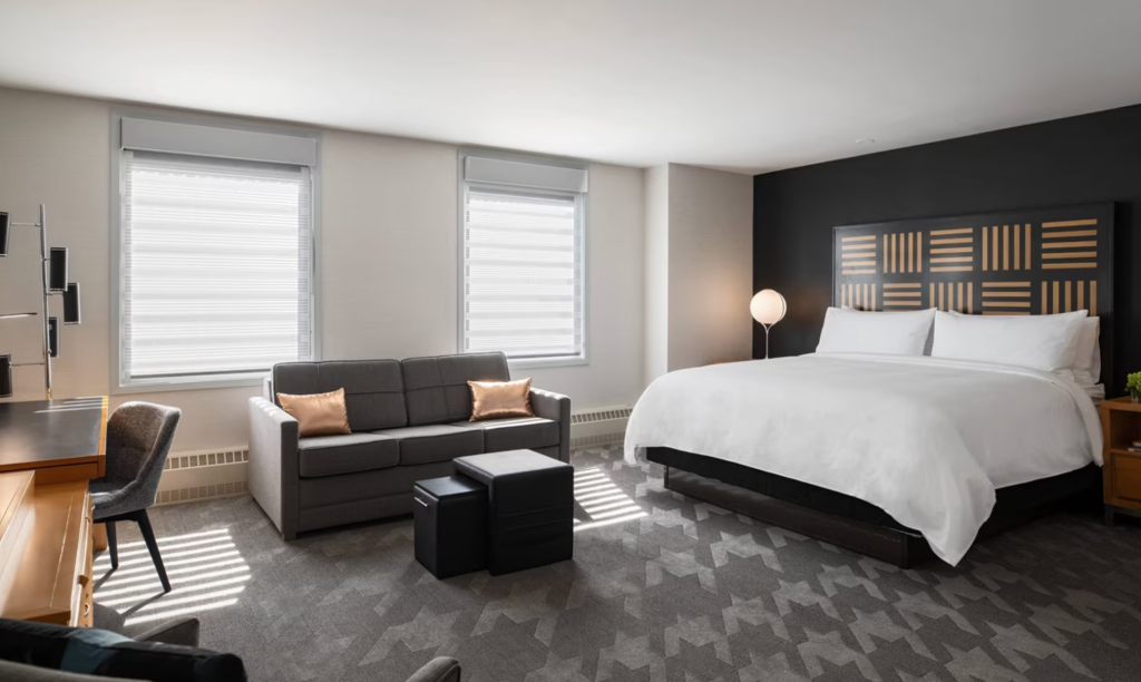 Contemporary hotel guest room with geometric headboard art and gray patterned carpet