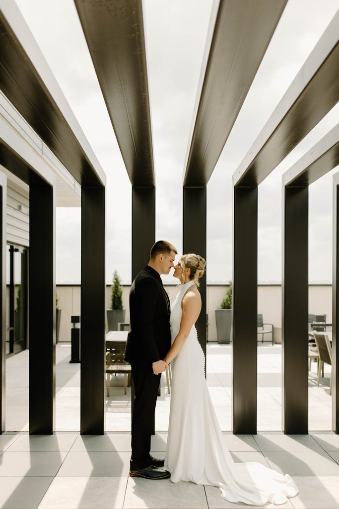 Newlyweds pose under modern geometric pergola on outdoor patio with city views