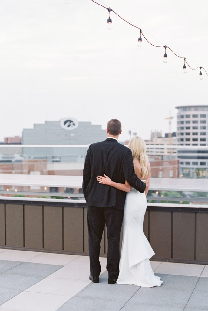 Bride and groom embracing on rooftop terrace overlooking downtown cityscape at dusk