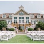 White folding chairs arranged on lawn before elegant mansion venue with stone staircases and dormers