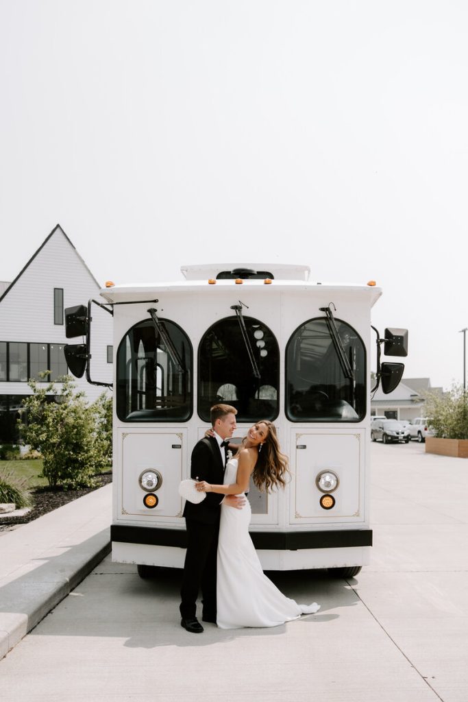 Bride and groom embrace in front of white vintage trolley at modern venue
