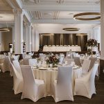 Elegant reception ballroom with white-draped tables, ornate ceiling details, and floral centerpieces