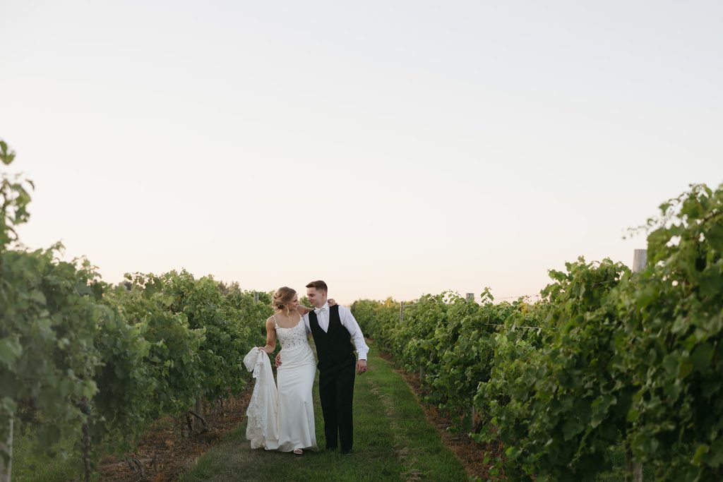 Bride and groom walking together through vineyard rows at sunset