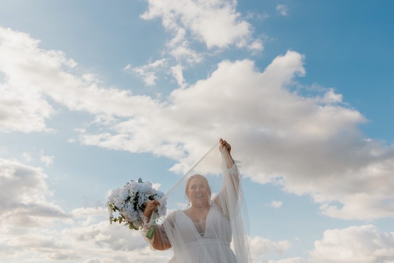 bride smiling through her veil in the sky