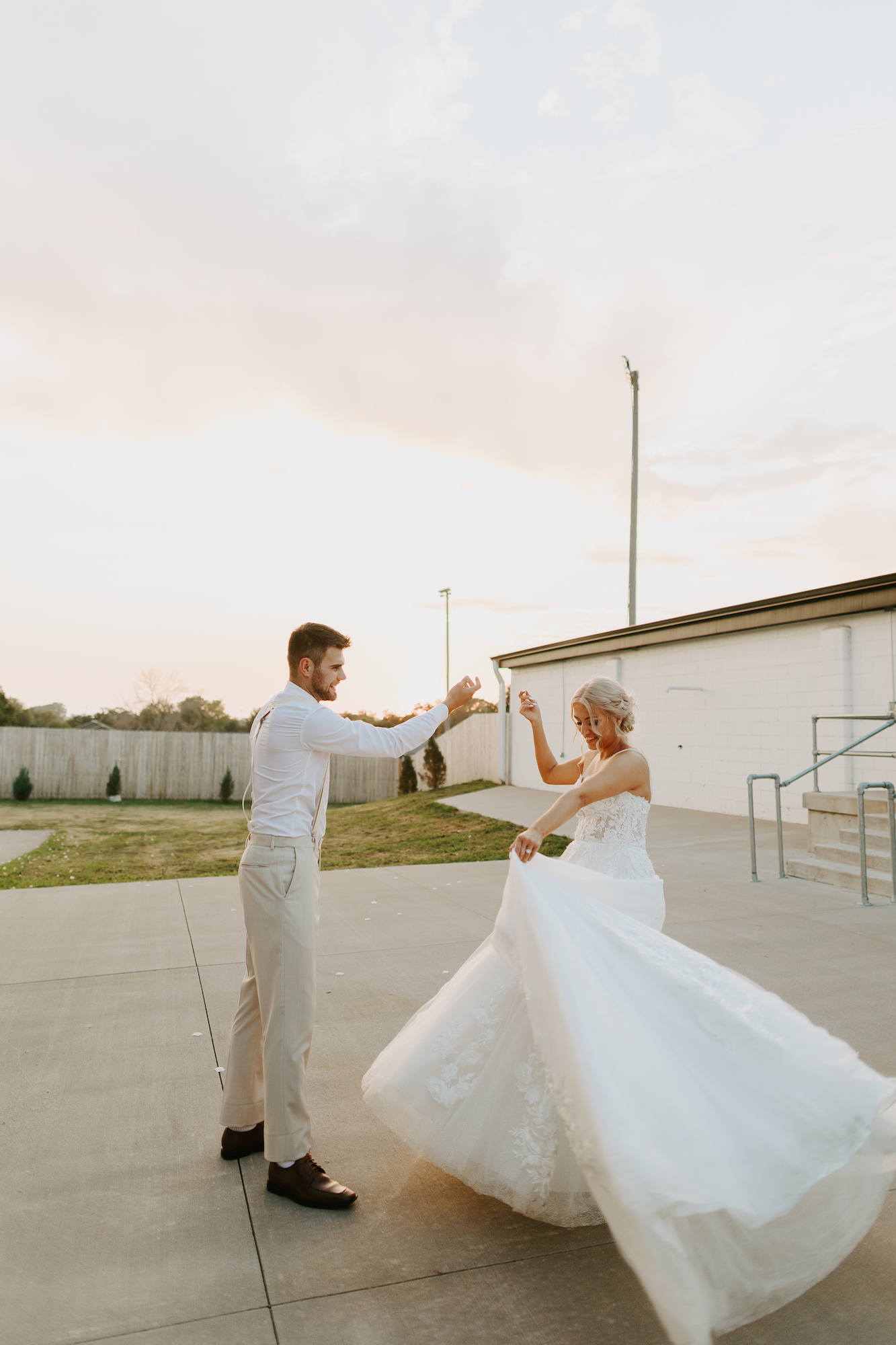 groom giving bride a spin in her wedding dress at sunset
