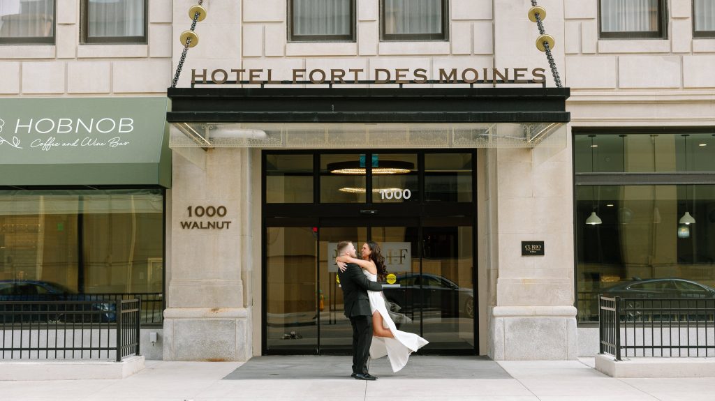 Groom dips bride in an embrace outside Hotel Fort Des Moines entrance in downtown Des Moines