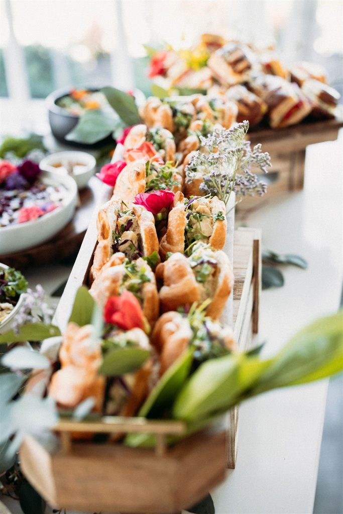 Tiered wooden display of gourmet appetizers garnished with fresh flowers and greenery