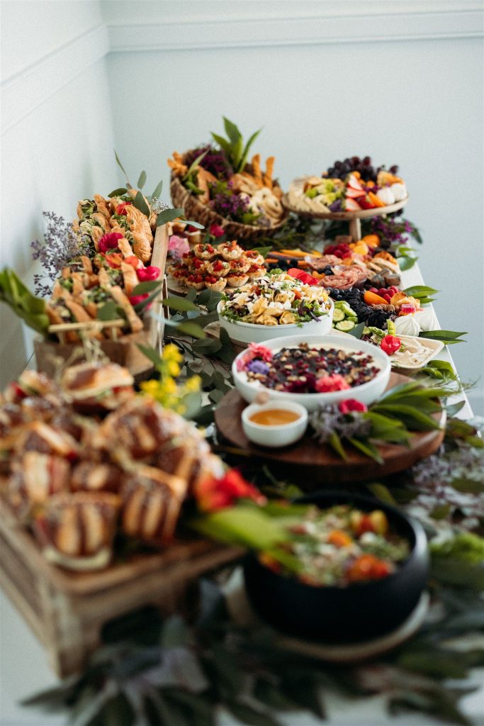 Multi-tiered grazing table featuring charcuterie boards, cheese platters, fresh fruits, and floral accents arranged on wooden stands