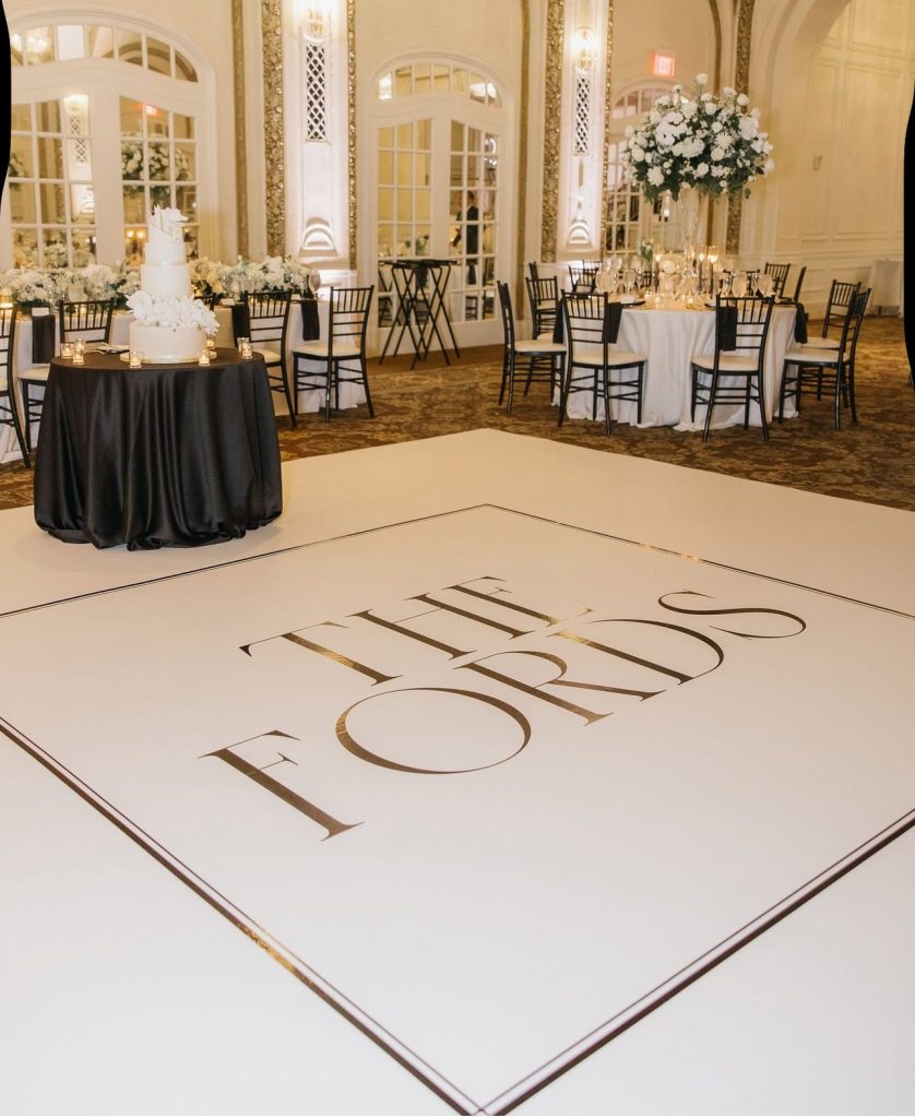 Custom dance floor monogram in elegant ballroom with white cake table and tall floral centerpieces