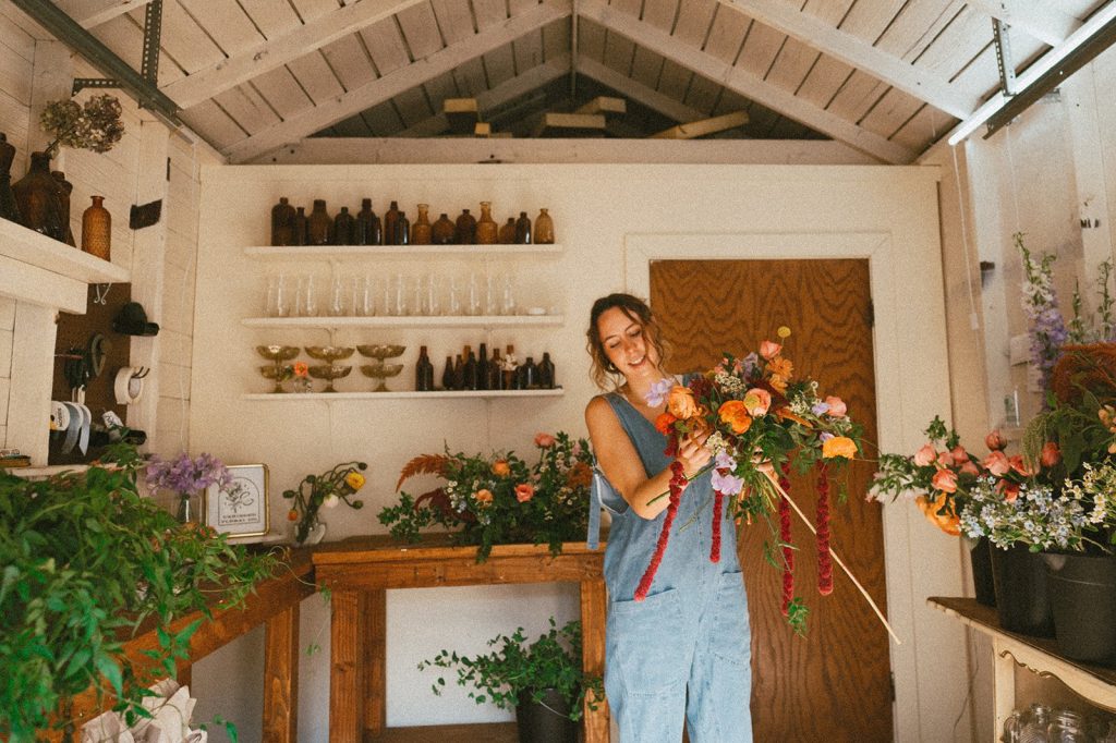 Florist arranging vibrant orange and pink blooms in rustic studio workspace