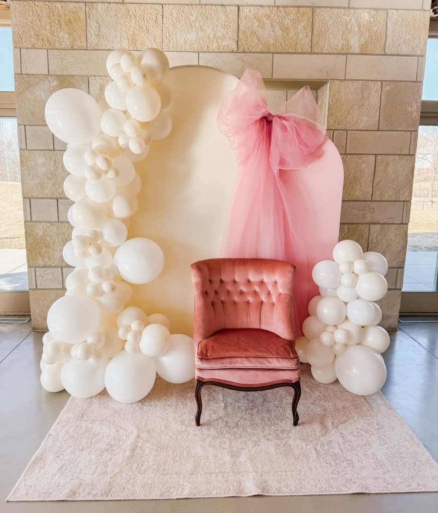 Pink velvet chair with white balloon garland and pink tulle backdrop creating photo booth display