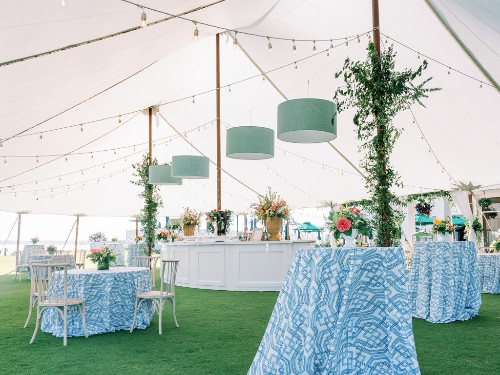 Tented reception space with blue patterned linens, turquoise drum chandeliers, string lights, and greenery-wrapped poles