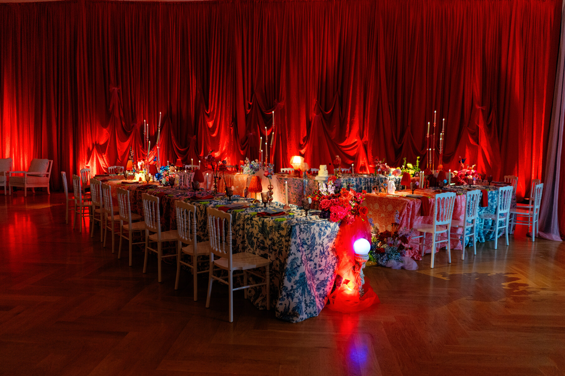 Dramatic wedding reception with red uplighting, draped curtains, and tables featuring colorful patterned linens