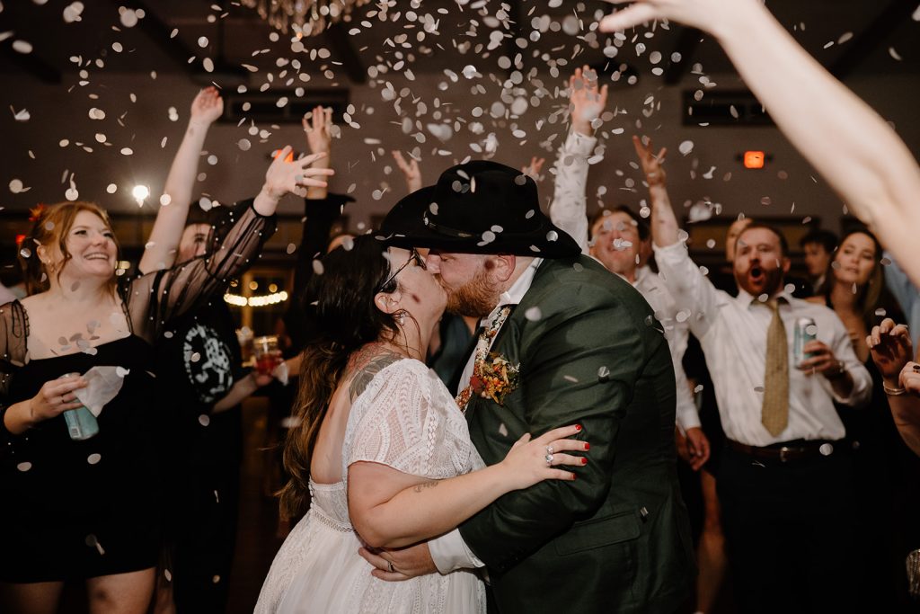 Newlyweds kiss during confetti toss send-off surrounded by cheering guests