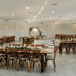 Tented wedding reception with string lights, round tables, wooden chairs, and rustic decor