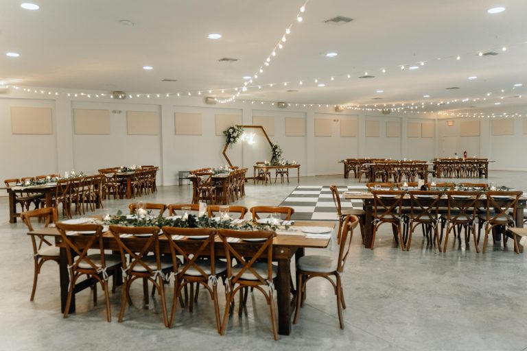 Tented wedding reception with string lights, round tables, wooden chairs, and rustic decor