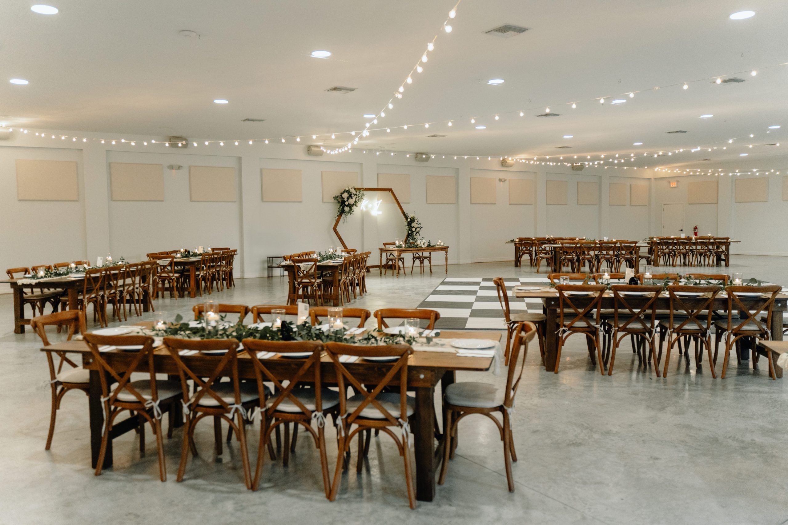 Tented wedding reception with string lights, round tables, wooden chairs, and rustic decor