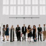 Live wedding band with twelve musicians holding instruments in white barn venue