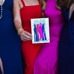 Wedding guests in colorful formal gowns hold custom fashion illustration of their dresses