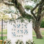 Seating chart display with eucalyptus garland and floral arrangements under Spanish moss-draped tree
