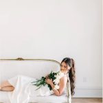 Bride in white dress reclining on vintage settee holding white and greenery bouquet