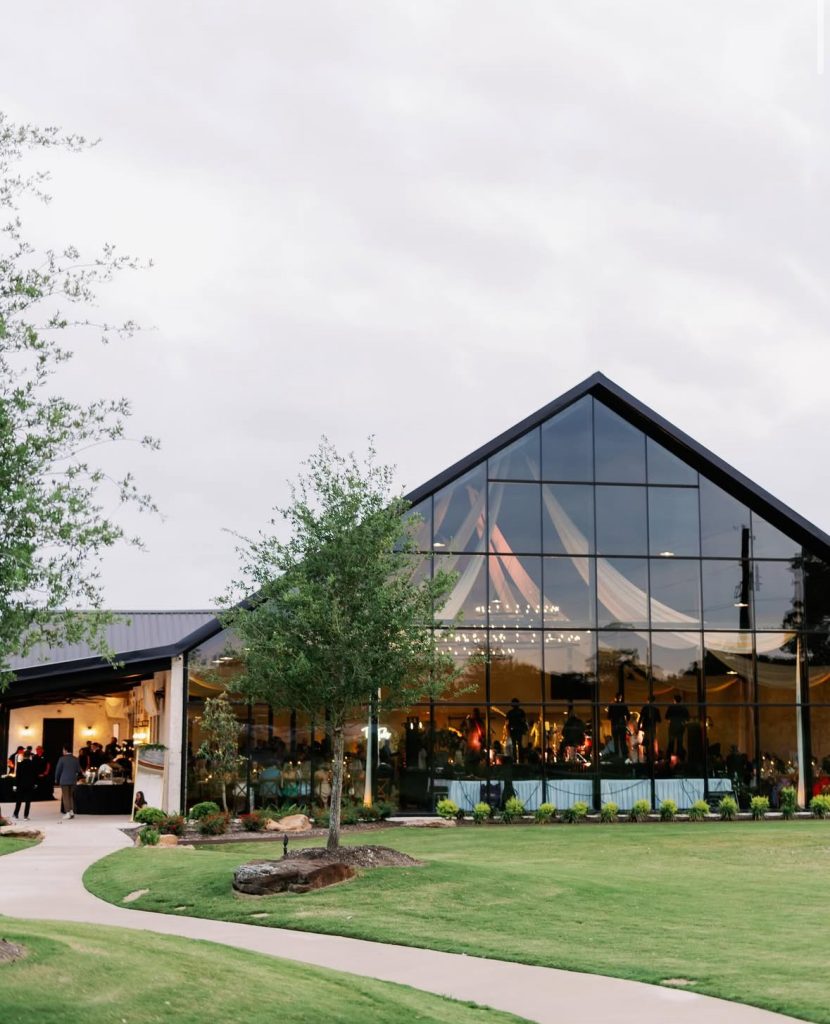 Modern glass chapel with peaked roof illuminated at dusk at Camp Hosea venue