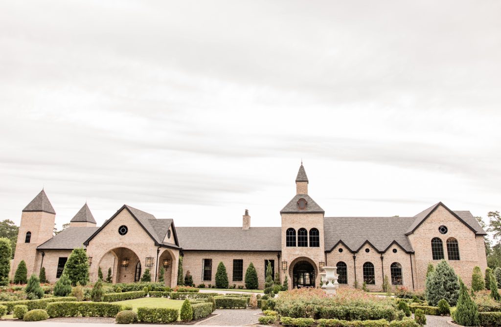 European-style brick manor with turrets and arched entrance surrounded by manicured gardens and topiaries