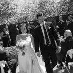 Newlyweds walk down the aisle hand-in-hand as guests applaud during outdoor ceremony