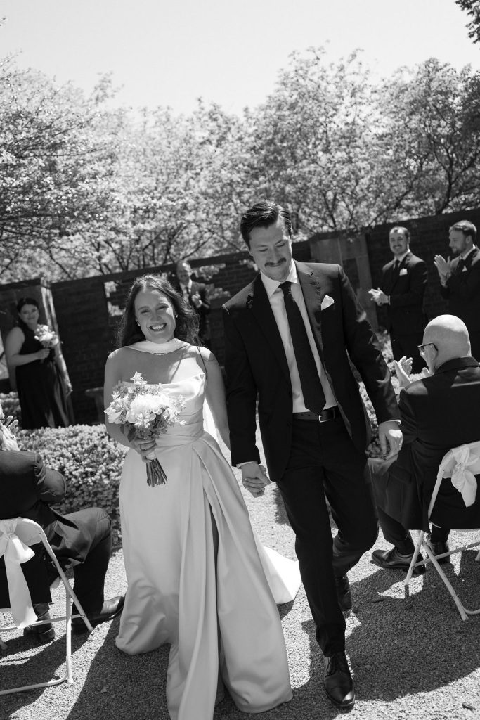 Newlyweds walk down the aisle hand-in-hand as guests applaud during outdoor ceremony
