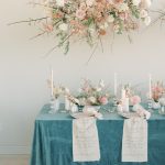 Romantic tablescape with teal velvet linen, blush blooms, taper candles, and calligraphy runners