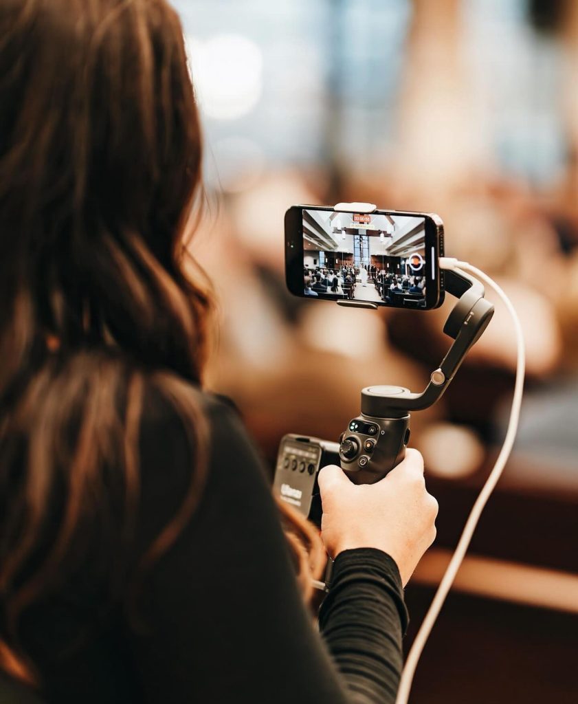Guest using smartphone gimbal stabilizer to record ceremony in elegant venue