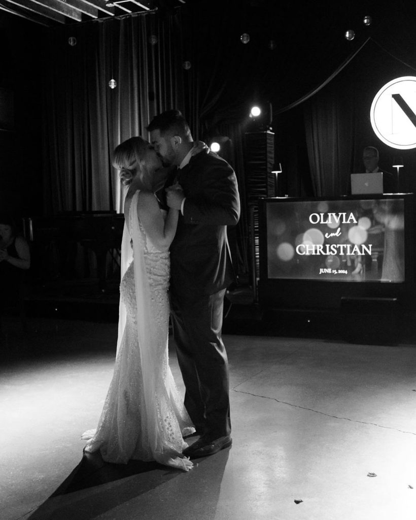 Bride and groom sharing first dance in dramatic spotlight with personalized projection screen behind them