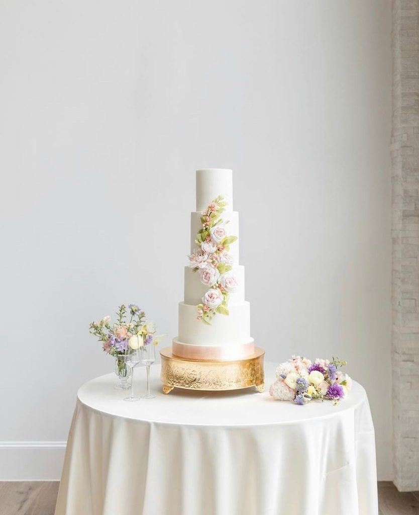 Four-tier white wedding cake adorned with delicate sugar flowers on gold cake stand