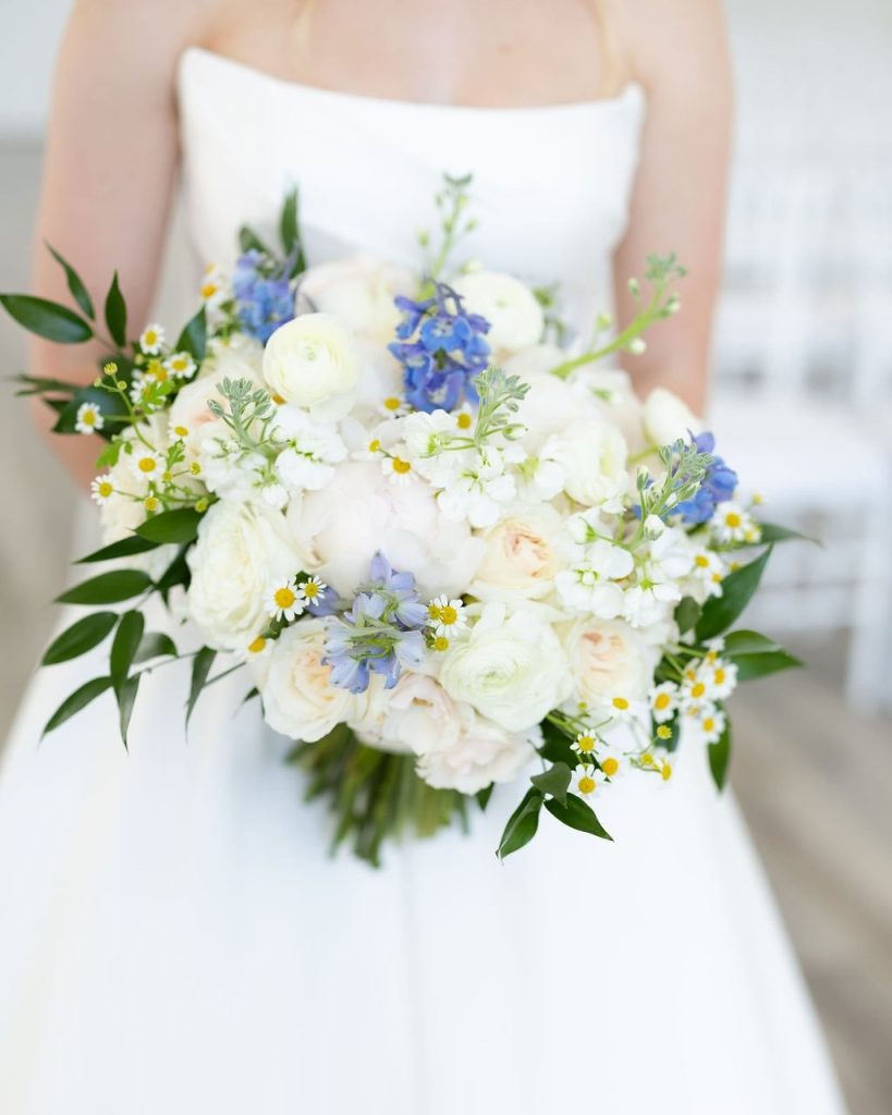 Bride holding white and blue wildflower bouquet with daisies in strapless wedding gown