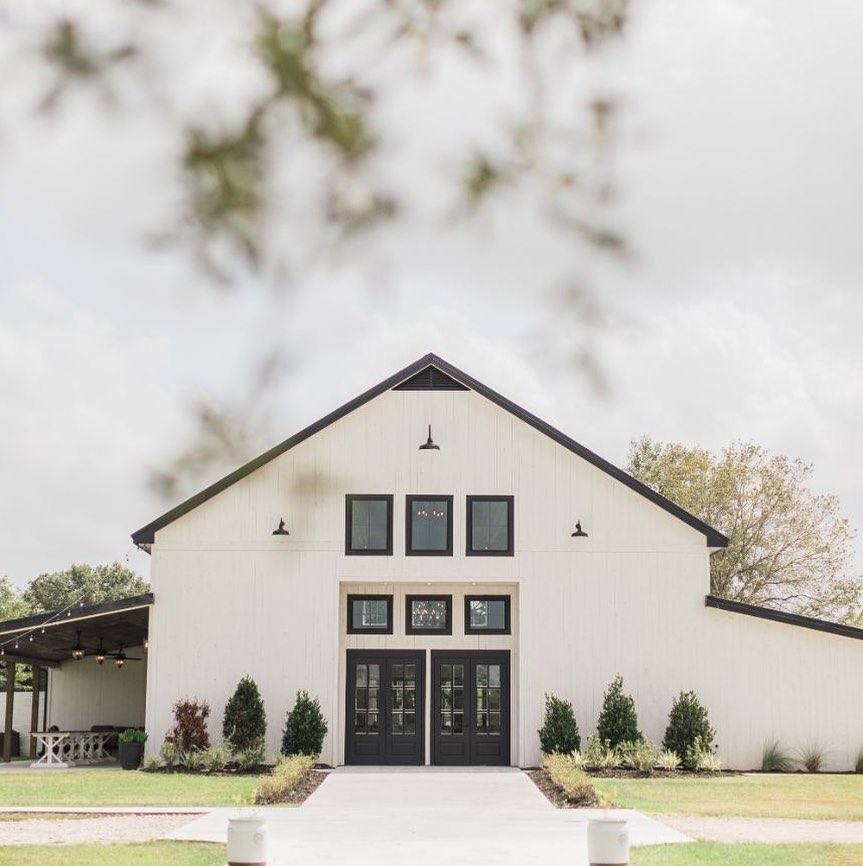 Modern white barn-style venue with black trim and symmetrical landscaping