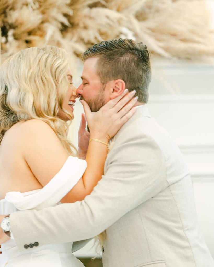 Newlyweds sharing an intimate moment on sandy beach with pampas grass in background