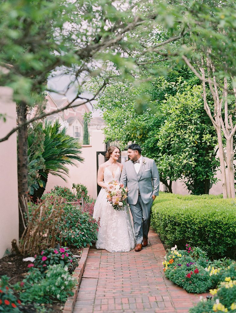 Newlyweds stroll hand-in-hand along brick garden pathway surrounded by lush greenery