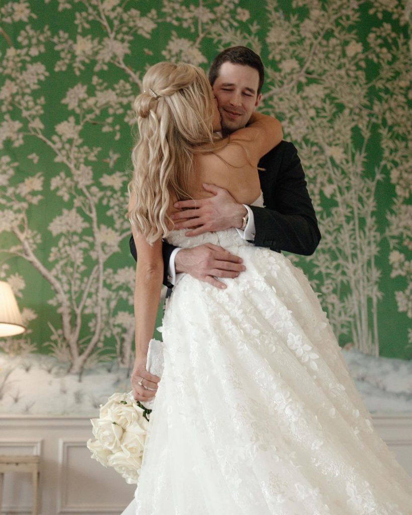Bride and groom embrace in sparkly white wedding dress against green floral wallpaper backdrop