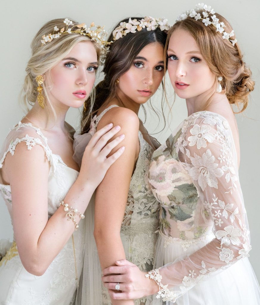Three brides wearing floral crowns and lace gowns in romantic bridal portrait