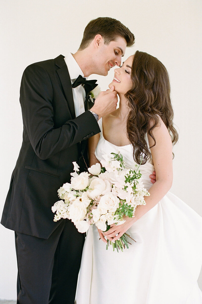 Newlyweds kissing while bride holds white and green bouquet