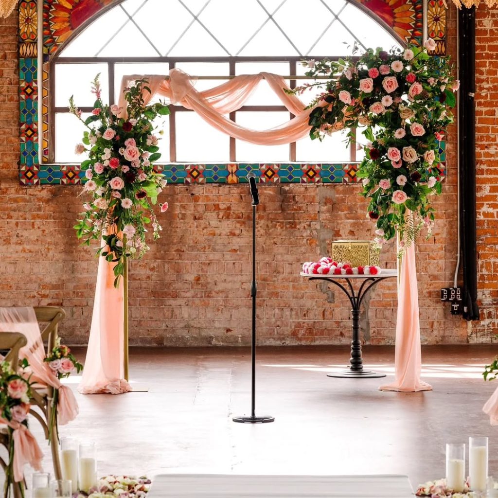 Floral wedding ceremony arch with blush and coral arrangements in industrial brick venue