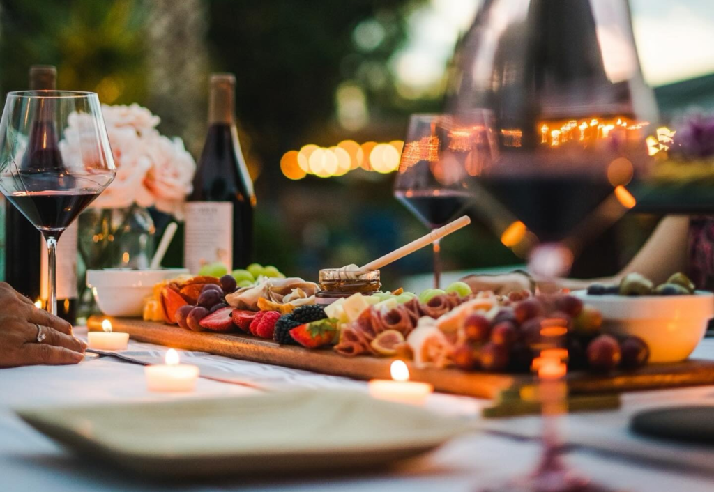 Evening charcuterie board with wine glasses, fruit, cheese, and meats illuminated by candlelight