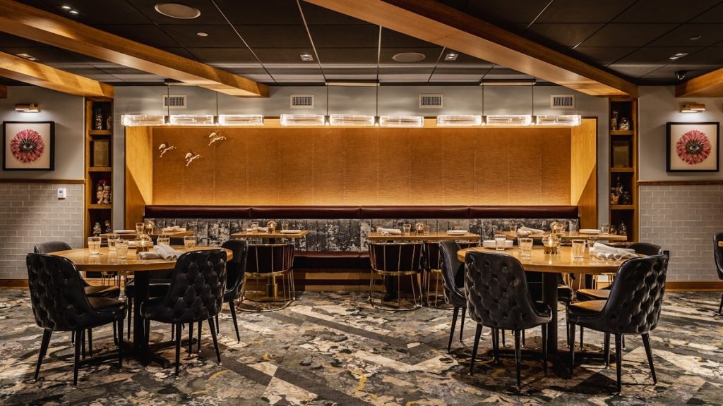 Private dining room with black tufted chairs around round tables, gold geometric wall panel, and patterned carpet