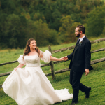Bride and groom holding hands in a field with a trees and a mounain view