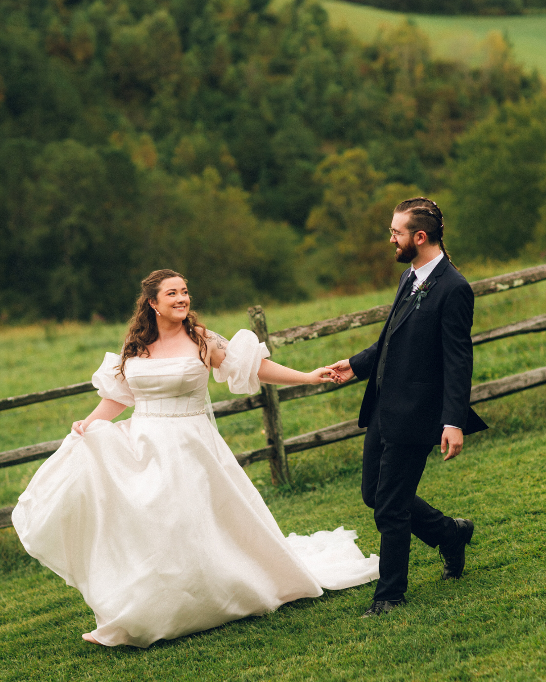Bride and groom holding hands in a field with a trees and a mounain view