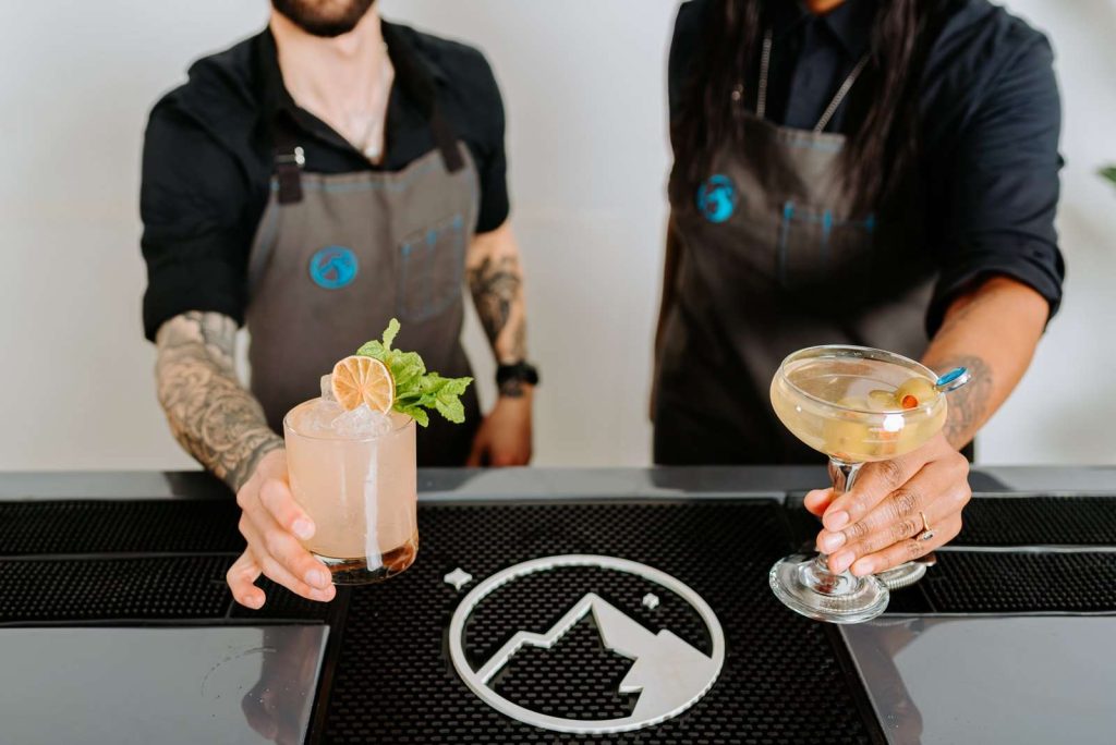 Peak Beverage bartenders presenting craft cocktails with citrus and mint garnishes at modern bar