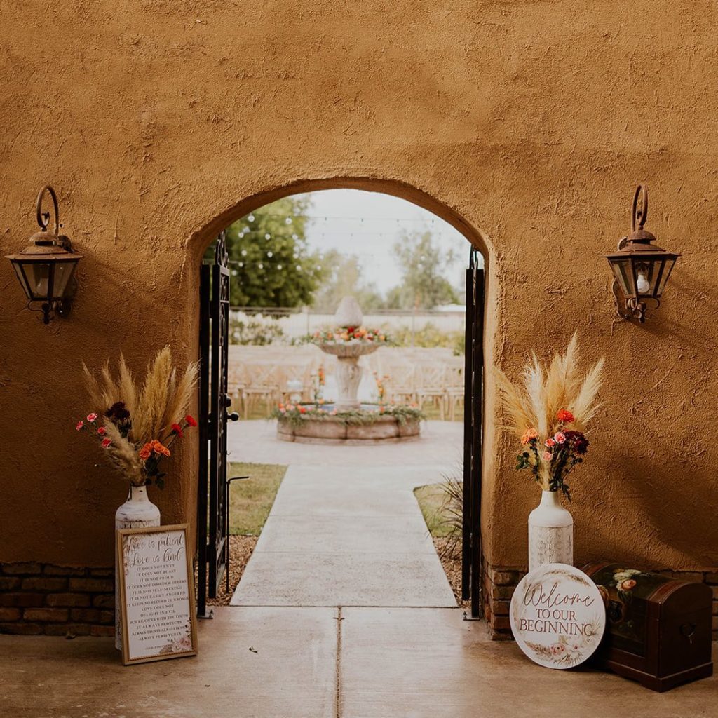 Arched doorway framed by golden stucco walls and lanterns, opening to outdoor wedding ceremony space in Mesilla